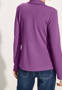 Purple long-sleeve shirt with a relaxed fit and a collar, paired with blue denim jeans featuring back pockets and stitching details.