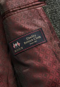 Interior de un blazer de lana con un forro rojo intenso que presenta un patrón repetido de flores. La etiqueta dice "MOON Quality British Cloth Since 1837."