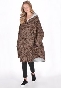 Barna és fekete leopárdmintás poncsó szürke kapucnival. Széles ujjakkal, laza szabással és hosszabb hátsó szegéllyel rendelkezik. Fekete nadrág felett viselve.