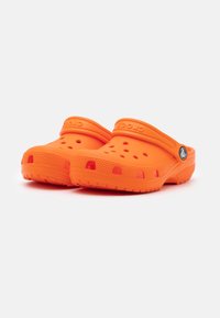 Orange Crocs-tofflor gjorda av lätt material, med ventilationshål, en bakrem och strukturerade sulor för grepp.