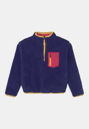 Pull-over en polaire marine avec un col et un ourlet jaunes, doté d'une poche poitrine zippée rose et d'un petit logo sur la poche. Ouverture zippée sur le devant.