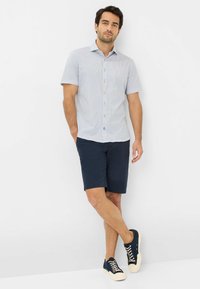 Wit shirt met korte mouwen en patroon, met marineblauwe accenten, gecombineerd met marineblauwe shorts en marineblauwe sneakers met beige veters en accenten.
