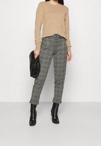 Maglione beige a maniche lunghe abbinato a pantaloni a quadri grigi e stivaletti neri con tacco, mentre tiene una borsa nera strutturata.