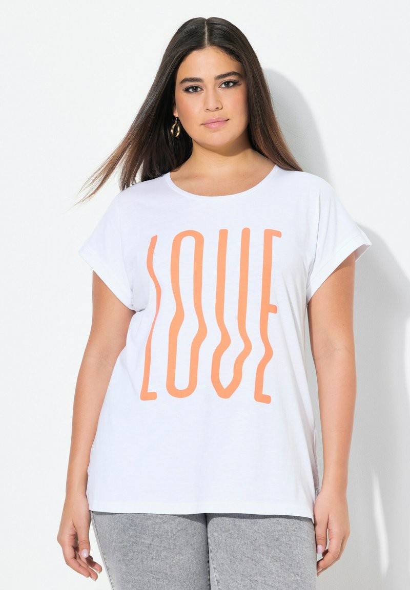 Witte korte mouwen t-shirt met oversized oranje "LOVE" tekstontwerp. Zachte stof, ronde halslijn, losse pasvorm. Gecombineerd met grijze jeans.