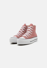 High-top sneakers in soft pink canvas with white laces, black stripe, and textured rubber sole. Features a white toe cap and soft lining.