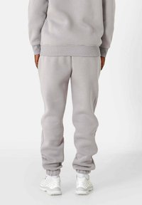 Pantalon de survêtement gris et sweat-shirt avec poignets et ceinture côtelés, assortis à des chaussures de sport blanches. Le tissu semble doux et confortable.