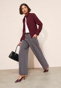 Bordowa koszula zapinana na guziki, biała bluzka, szare szerokie spodnie oraz bordowe szpilki. Czarna torebka uzupełnia całość.