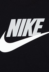 Tissu noir avec un grand logo blanc "NIKE" et un graphique de swoosh, présentant une texture lisse et un design audacieux et moderne.