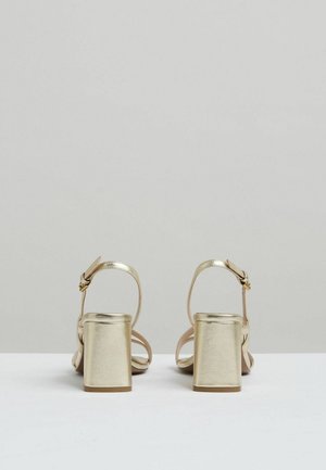 Arany fémes tömbsarkú szandál boka pánttal, sima textúrával és nyitott hátsó kialakítással.