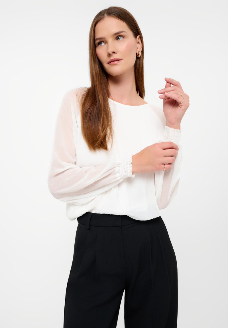 Witte blouse met doorschijnende lange mouwen en elastische manchetten, gecombineerd met hoog rijdende zwarte broeken. Soepele stof met een ontspannen pasvorm.