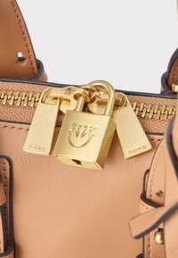 Borsa a mano in pelle tan con hardware dorato, dotata di un lucchetto, doppie zip e una superficie texture. Logo del marchio visibile sugli accessori.