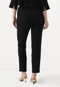 Zwarte broeken met een elastische tailleband, slim fit, gladde textuur en knielange snit. Draag met lichtgekleurde hakken.