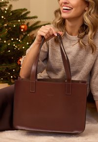Borsa a tote in pelle marrone con due manici piatti, forma rettangolare, texture liscia, design minimalista e dettagli del logo sottili sul fronte.