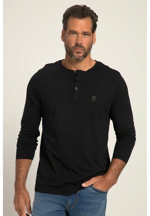 Maglietta nera a maniche lunghe in cotone, con colletto henley e tre bottoni, e un piccolo logo sul petto. Abbinata a jeans blu.