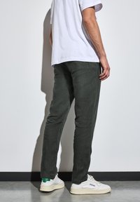 Tummanvihreät housut, jotka on valmistettu teksturoidusta kankaasta ja joissa on kapeneva malli, yhdistetty valkoisiin lenkkareihin, joissa on vihreitä yksityiskohtia. Yksinkertainen valkoinen t-paita.