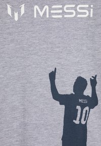 Camiseta de algodón gris con la silueta oscura de un jugador con las manos levantadas, y el nombre "MESSI" y el número "10" impresos en ella.