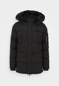 Svart vadderad jacka med pälsfodrad huva. Har fyra framfickor och en sidoficka med dragkedja. Tillverkad av slät, vattenavvisande material.