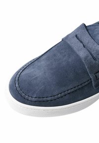 Mocassini in suede blu navy con suola in gomma bianca. Presentano dettagli cuciti e una superficie liscia, progettati per un uso informale.