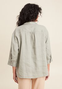 Lichtgroene linnen shirt met een relaxed fit, lange mouwen opgerold en een achterzijde met een gathered detail. Heeft knoopmanchetten en een kraag.