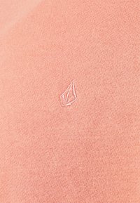 Lys koralstrikket sweater med tekstureret finish og et lille hvidt broderet logo på venstre side.