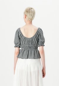 Top in gingham bianco e nero con maniche a sbuffo, vita elastica e schiena scoperta. Abbinato a una gonna bianca fluente. Texture liscia.