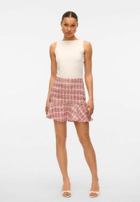 Débardeur beige ajusté associé à une jupe à volants rose à motifs. La jupe présente un motif en croix dans des nuances de rose plus foncé et des accents noirs.