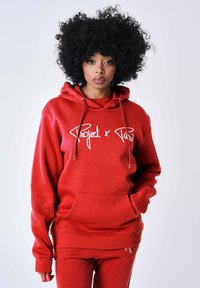 Sudadera roja con capucha, con un bolsillo delantero y cordones, que presenta el texto impreso en blanco "Project x Paris". El material parece suave y texturizado.