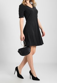 Zwarte jurk met korte mouwen en een V-hals, met een uitlopende rok. Gecombineerd met zwarte hoge hakken en een kleine zwarte handtas. Soepele stoftextuur.