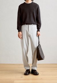 Grauer Wollpullover, hellgraue Hose, schwarzer Gürtel und schwarze Lederschuhe. Tragend eine schwarze Leder-Tasche. Einfaches Design, ohne Muster.