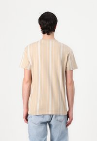 Beige short-sleeve t-shirt with white vertical stripes, featuring a crew neckline and a relaxed fit. Smooth cotton fabric.