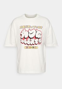 Bílé oversized tričko s barevným japonským textem a výrazným grafickým designem v červené, černé a bílé barvě na přední straně, vystavené na jednobarevném pozadí.