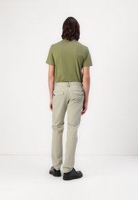 Olivenfarbener T-Shirt mit kurzen Ärmeln, kombiniert mit hellgrauen Hosen; die Hosen haben zwei Gesäßtaschen und einen Kordelzug, abgerundet mit schwarzen Schuhen.