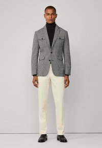 Gray houndstooth blazer with two front pockets, black turtleneck, cream trousers, and black shoes. Smooth texture, fitted design.