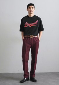 Μαύρο βαμβακερό t-shirt με κόκκινο λογότυπο "Dsquared", σε συνδυασμό με μπορντώ κομμένες παντελόνες. Ζώνη με τετράγωνη αγκράφα και γυαλιστερές μαύρες παπούτσια.