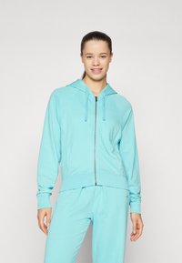 Svijetloplavi zip-up dukserica s kapuljačom na vezanje, raglan rukavima i rebrastim rubom. Izrađena od mekog materijala, u kompletu s odgovarajućim hlačama.