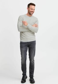Pull gris côtelé, jean slim noir et chaussures noires. Le pull présente un petit accent multicolore sur la poitrine gauche.