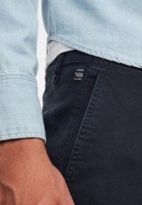 Jeansjacka med ärm i ljusblått tyg, i kombination med mörkblå byxor med en silverfärgad logotagg, som visar strukturerat tyg och ren sömnad.