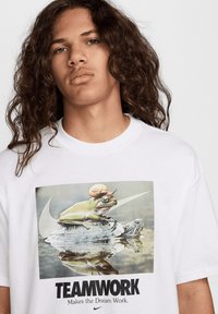 Camiseta blanca con un gráfico de una rana con un caracol en la cabeza sentada sobre una tortuga, con el texto "El TRABAJO EN EQUIPO hace que el sueño funcione" debajo.