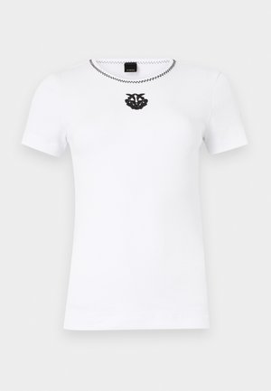 White short-sleeve ribbed knit top with black zigzag neckline stitching and black decorative emblem centered below collar.