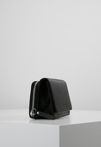 Czarny portfel ze skóry o fakturowanym wykończeniu, wyposażony w zamek błyskawiczny, prostokątny kształt oraz subtelne wytłoczone logo.