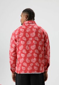Rood overhemd met patroon, voorzien van witte paisley-ontwerpen, gemaakt van een gestructureerde stof met lange mouwen en een kraag.