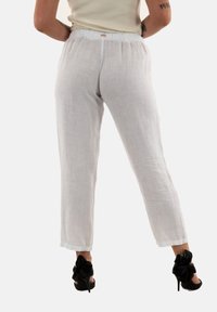 Pantaloni in lino bianchi dalla vestibilità rilassata, con una vita elastica e orli arrotolati, abbinati a scarpe nere con tacco alto e fiocchi.