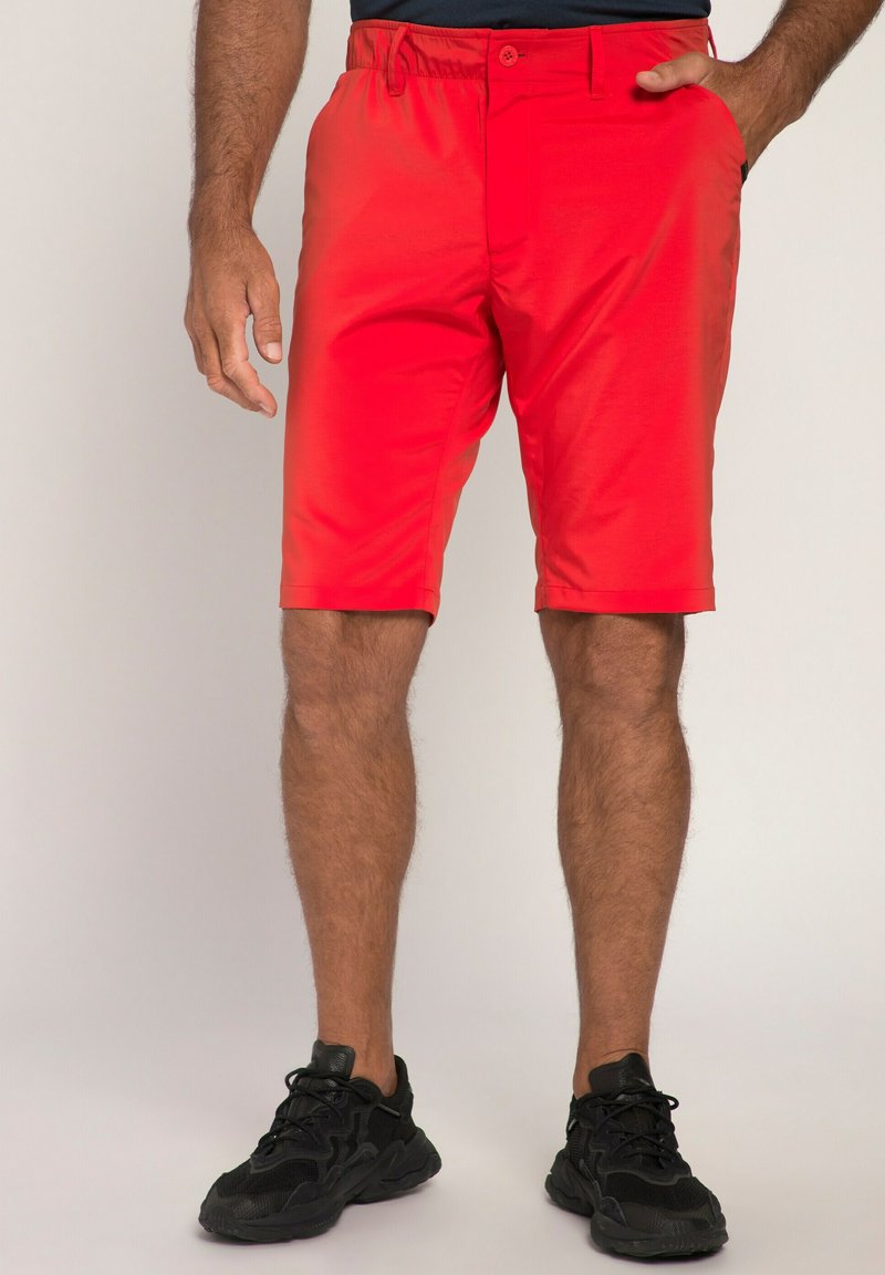 Rode shorts met een gladde textuur, een knoopsluiting in de taille en zijzakken, gecombineerd met zwarte sportschoenen met een gestructureerd ontwerp.