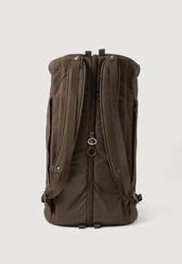 Mochila de tecido castanho com textura acolchoada, duas alças ajustáveis, um fecho central e bolsos laterais. Detalhes em metal visíveis.