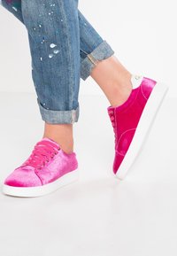 Baskets en velours rose avec accents blancs au talon, bout rond et semelle plate blanche. Les lacets passent par des œillets métalliques pour un ajustement sécurisé.