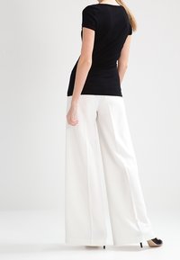Černý krátký top s krátkými rukávy v kombinaci s širokými bílými kalhotami. Souprava má elegantní design a hladkou texturu, zvýrazněnou kontrastními barvami.