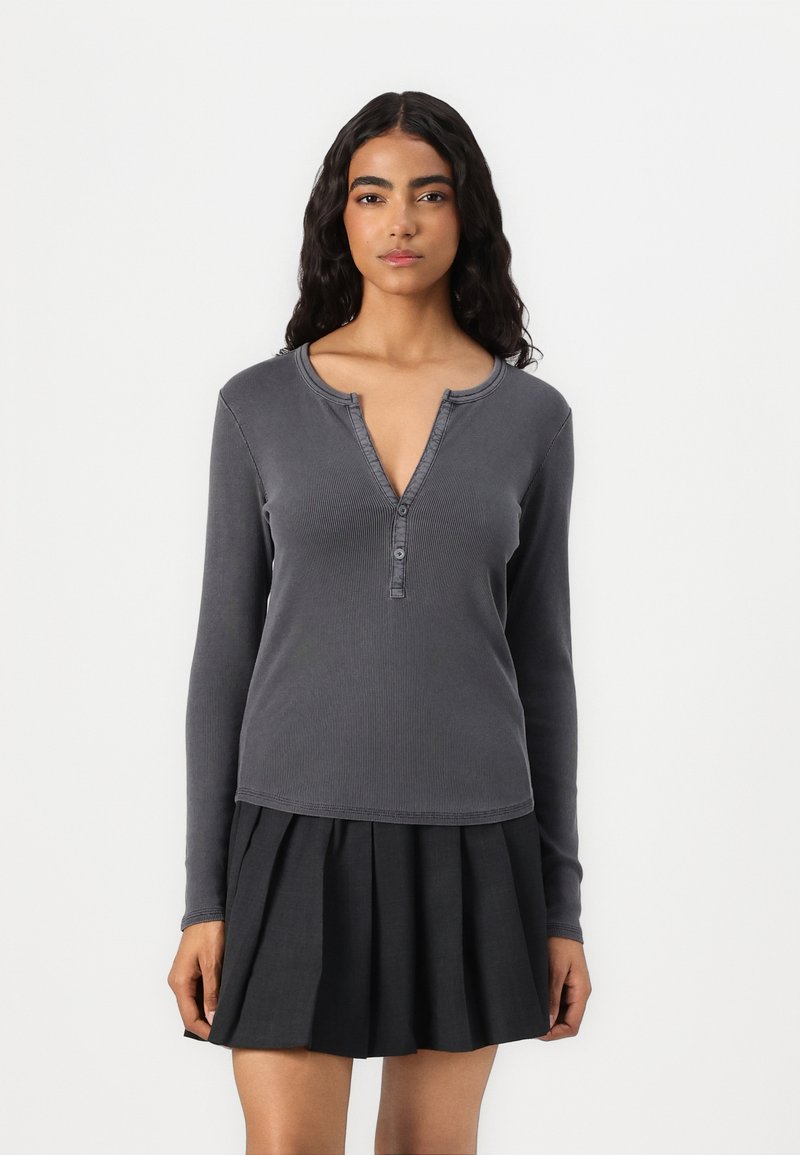 Grå ribbet langermet topp med henley-utsnitt, med tre knapper. Kombinert med et svart plissert skjørt.