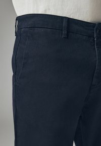 Pantaloni blu navy realizzati in tessuto morbido. Presentano una vita standard con passanti per cintura. Il design include una vestibilità classica con tasche laterali.