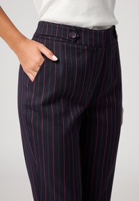 Donker gestreepte broek heeft een op maat gemaakte stijl met zijzakken en twee knopen op de tailleband, wat zorgt voor een slanke, gestructureerde pasvorm.