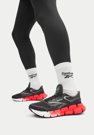 Czarne buty sportowe z teksturowanym wierzchem i wyraźnym czerwonym amortyzatorem. Posiadają logo Reebok, lekką konstrukcję i zaokrąglony kształt.